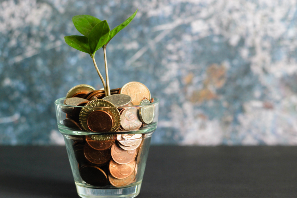 A glass with coins in it. A small plant is growing out of the glass of coins.